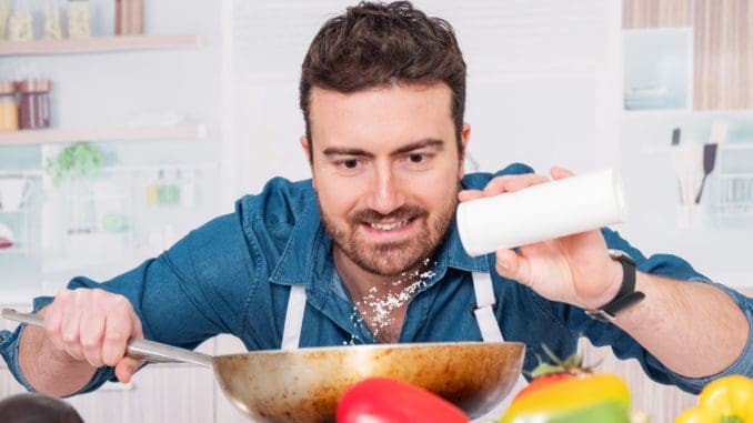 One man is cooking in his kitchen and adding salt