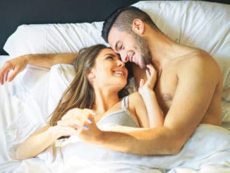 Young loving couple lying in bed cuddling looks each other under white blankets