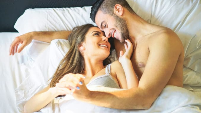Young loving couple lying in bed cuddling looks each other under white blankets