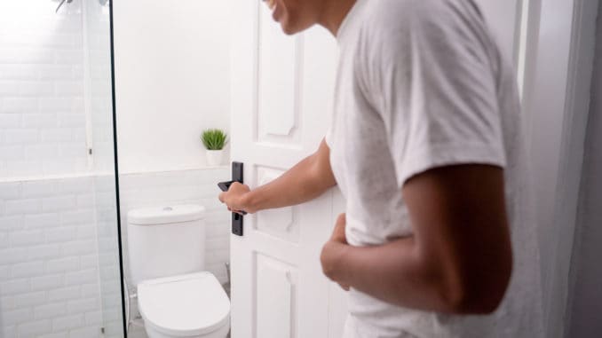 Man opening the toilet door and hold his stomach ache