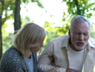 Senior man suffering sharp back pain, walking in park, caring wife helping him, stock photo