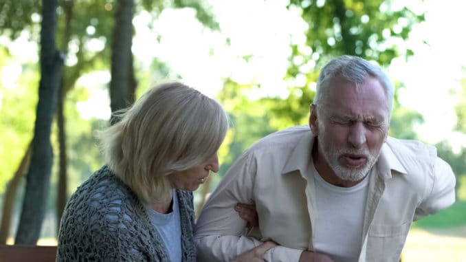 Senior man suffering sharp back pain, walking in park, caring wife helping him, stock photo