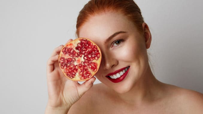 Beauty woman with orange pomegranate cut in half over white background. Attractive fresh vitamin concept