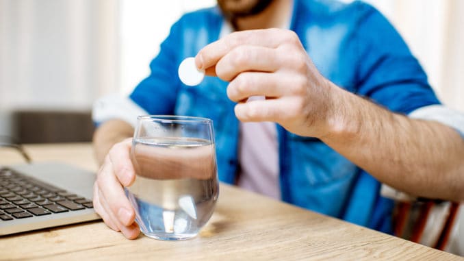 Man taking antipyretic or analgesic pills feeling bad while working on the laptop at home