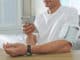 Man checking blood pressure with modern monitor and smartphone at table indoors, closeup. Cardiology concept