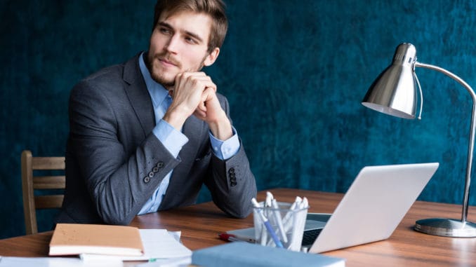 Shot of young man sitting at table looking away and thinking. Thoughtful businessman sitting in office