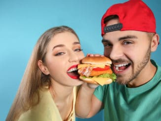 Happy couple eating burger on color background