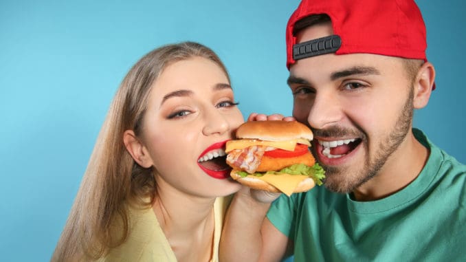 Happy couple eating burger on color background