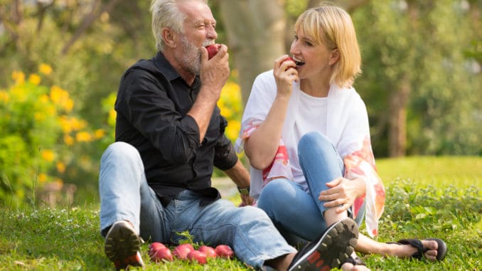 Happy senior couple relaxing in park eating apple together morning time.