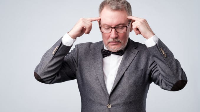 Senior man in suit and glasses holds fingers on temples, trying to remember or generate idea