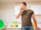 Young smiling handsome man bites organic green apple while cooking fresh fruits in the kitchen. Healthy eating. Vegetarian meal. Diet detox