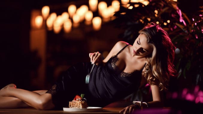 Young blonde woman eating strawberry cake desert in a cafe restaurant in the evening time celebrating birthday party