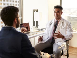 Man Having Consultation With Male Doctor In Hospital Office