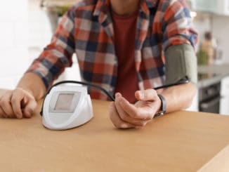 Man checking blood pressure with sphygmomanometer at table indoors, closeup.