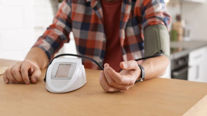 Man checking blood pressure with sphygmomanometer at table indoors, closeup.