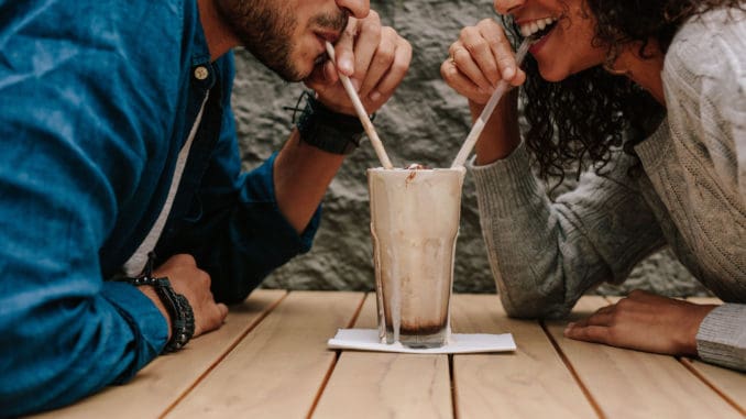 dreamstime_m_145095251 Happy young couple in love at cafe drinking a milkshake from same glass.