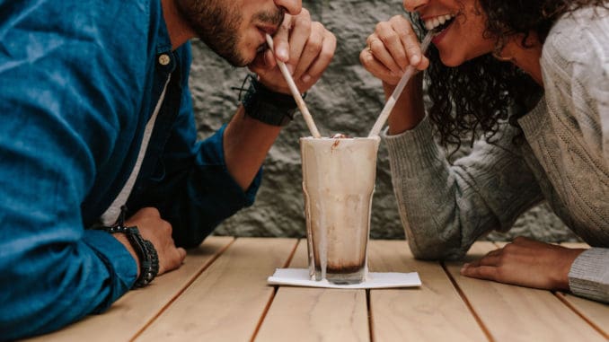 Happy young couple in love at cafe drinking a milkshake from same glass.