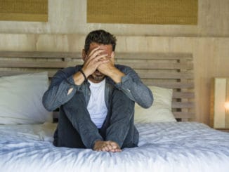 Lifestyle home portrait of young attractive stressed and depressed man sitting on bed worried and frustrated suffering depression crisis covering face with hands feeling desperate and helpless