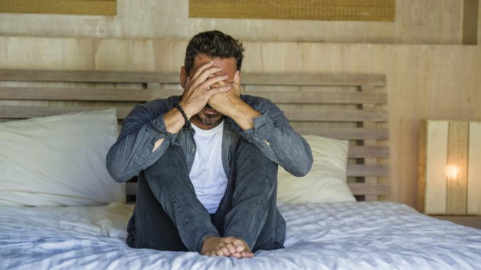 Lifestyle home portrait of young attractive stressed and depressed man sitting on bed worried and frustrated suffering depression crisis covering face with hands feeling desperate and helpless