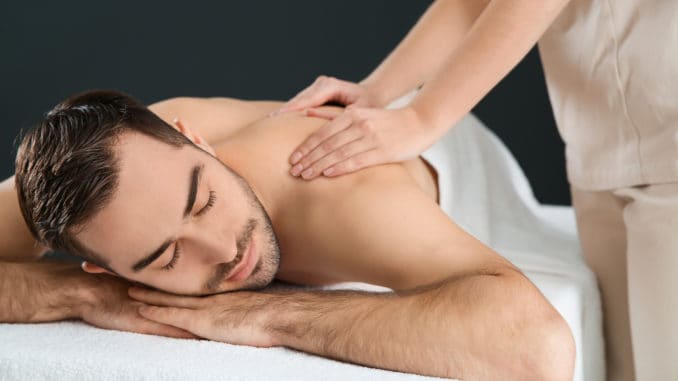 Handsome man receiving back massage on black background. Spa service