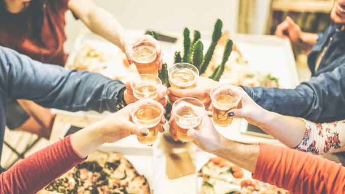 Group of friends enjoying dinner toasting with beers and eating take away pizza at home