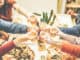 Group of friends enjoying dinner toasting with beers and eating take away pizza at home