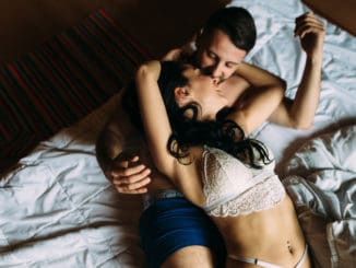 Stylish and passionate couple in their underwear kissing on the bed at home.