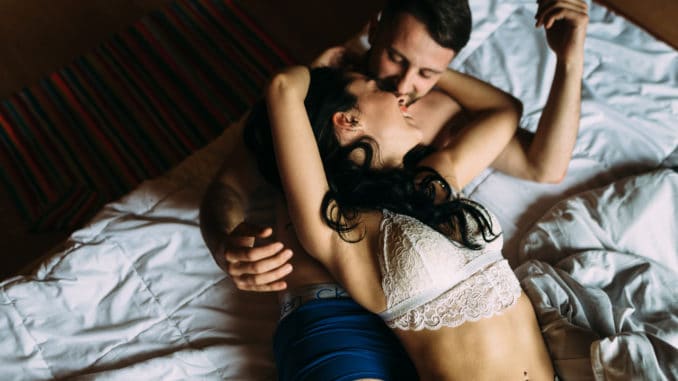 Stylish and passionate couple in their underwear kissing on the bed at home.