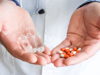 Concept of choice of therapeutic treatment - orange capsules with medication or injectable therapy in form of ampoules with medicinal substance. Doctor holds in one palm ampoules, in another capsules