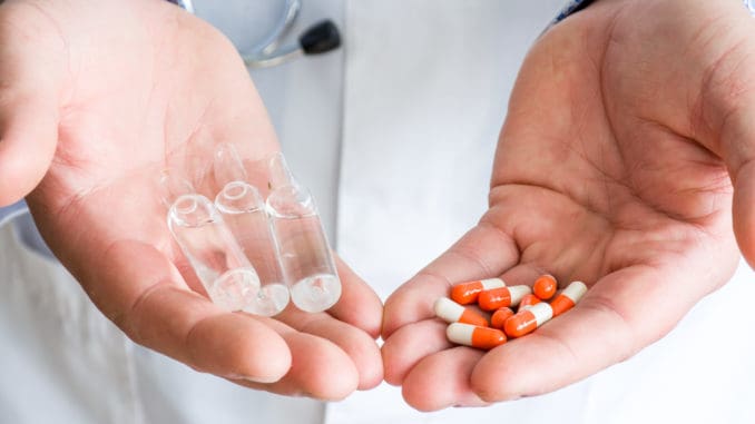 Concept of choice of therapeutic treatment - orange capsules with medication or injectable therapy in form of ampoules with medicinal substance. Doctor holds in one palm ampoules, in another capsules