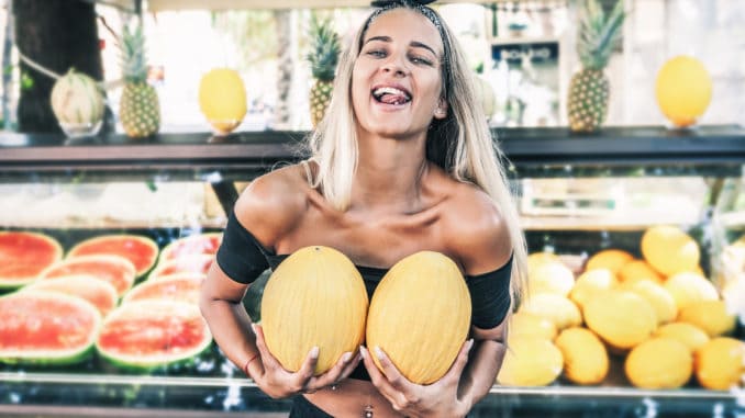 Young blonde woman holding two yellow melons in her hand