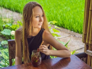 Young woman drinking cold tea with cinnamon in rice field.