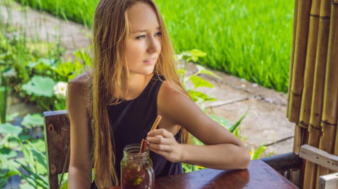 Young woman drinking cold tea with cinnamon in rice field.