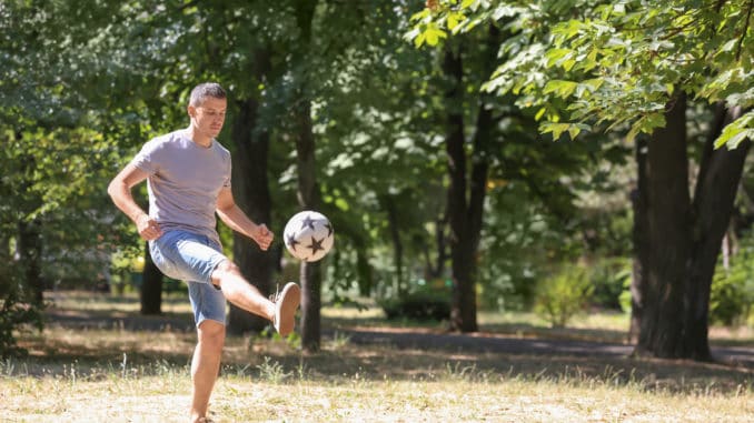 Handsome man playing football outdoors