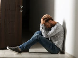 Depressed young man sitting on floor in dark corridor