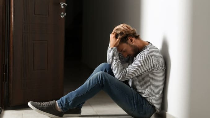 Depressed young man sitting on floor in dark corridor Depressed young man sitting on floor in dark corridor