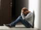 Depressed young man sitting on floor in dark corridor