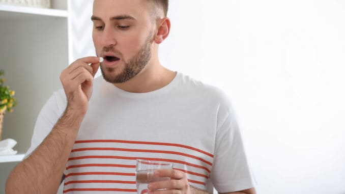 Young man ill with flu taking medicine at home