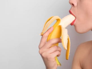 young woman eating banana on light background. Erotic concept