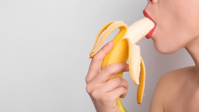 young woman eating banana on light background. Erotic concept