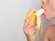 young woman eating banana on light background. Erotic concept