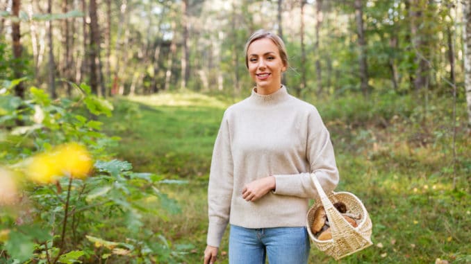 young woman with wicker basket and knife picking mushrooms in forest