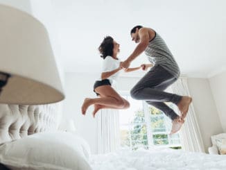 Man and women holding hands and jumping together on bed.
