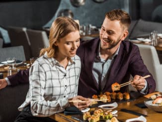 Attractive happy young adult couple eating sushi in restaurant