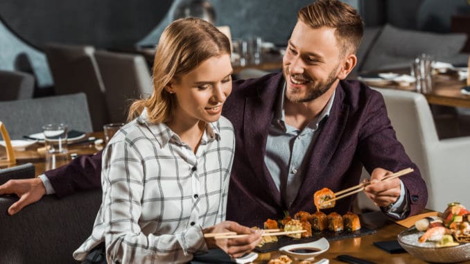 Attractive happy young adult couple eating sushi in restaurant