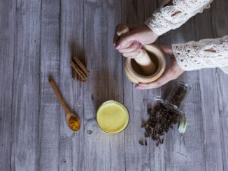Top view of woman hands with ingredients on table, wooden mortar, yellow turmeric, clove and green natural leaves. Close up, daytime