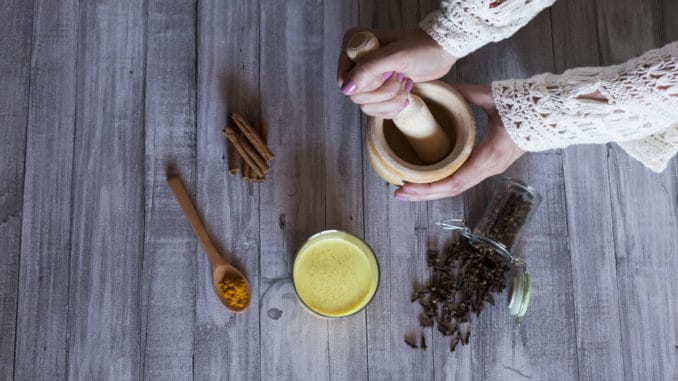 Top view of woman hands with ingredients on table, wooden mortar, yellow turmeric, clove and green natural leaves. Close up, daytime