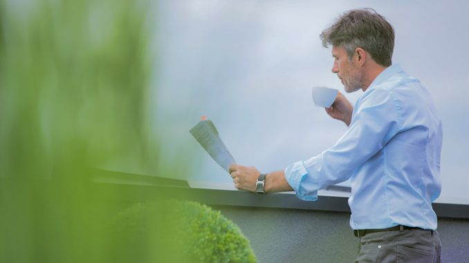 Senior business man reading his notes and enjoying a morning coffee whilst standing on his balcony