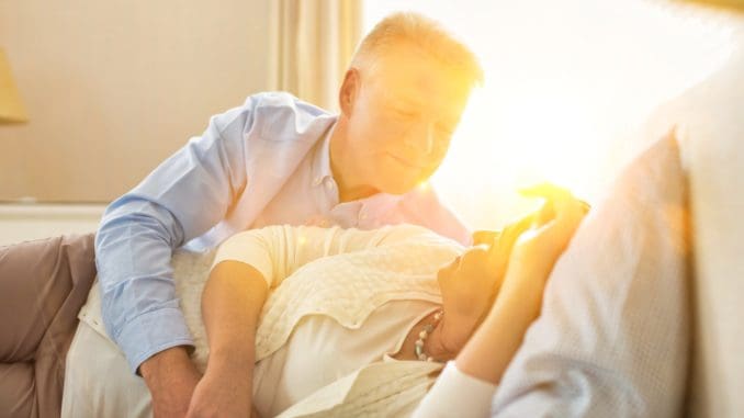 Sweet senior couple cuddling in bed with yellow lens flare in background
