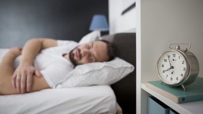 Man sleeping in his bedroom with alarm clock in foreground. It’s morning